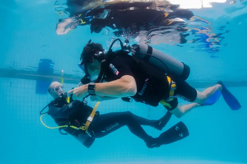 Deux plongeurs en formation s'entraînent dans une piscine bleu clair