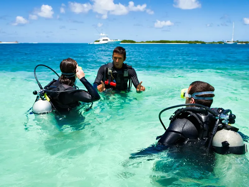 Trois plongeurs en combinaison discutent dans une eau turquoise claire