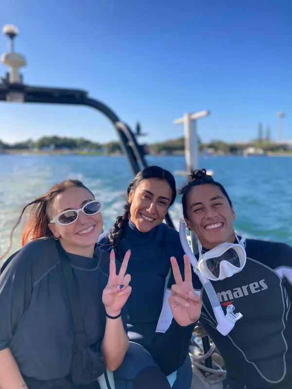 Trois femmes souriantes font des signes de la main sur un bateau
