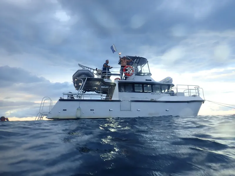 Bateau de plongée avec deux personnes sur le pont, ciel nuageux