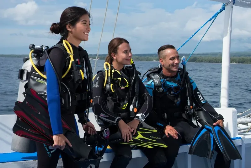 Trois plongeurs souriants équipés sur un bateau en mer
