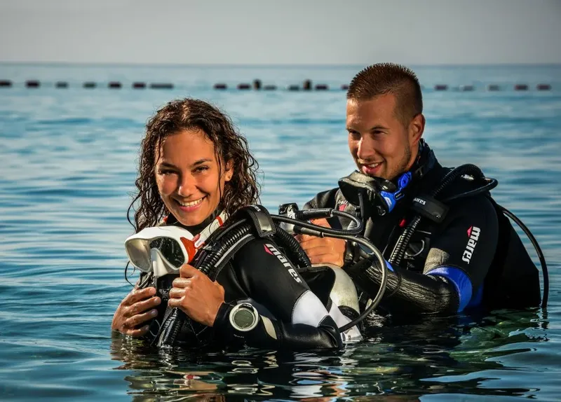 Deux plongeurs souriants en combinaison, équipés, dans l'eau claire