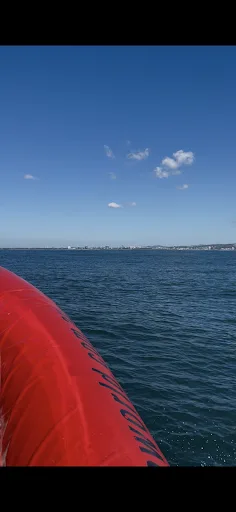 Vue mer depuis un bateau rouge, ciel bleu et côte au loin