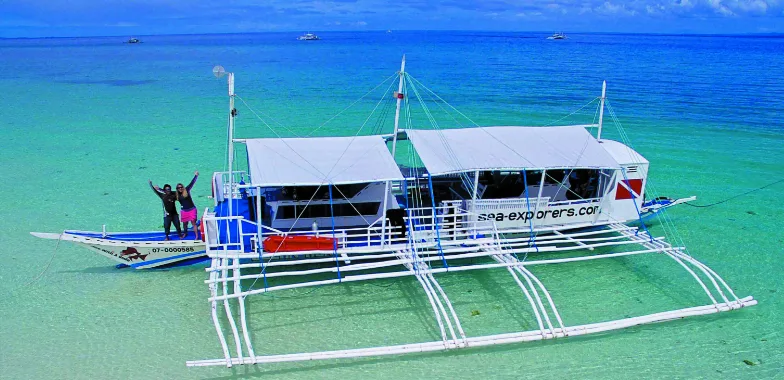 Bateau de plongée turquoise et blanc avec deux personnes souriantes à bord