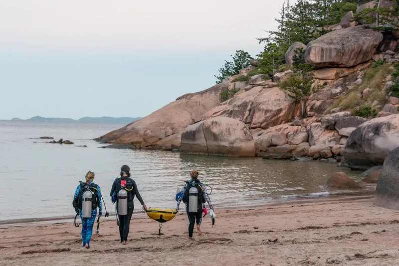 Trois plongeurs équipés marchent sur une plage vers la mer
