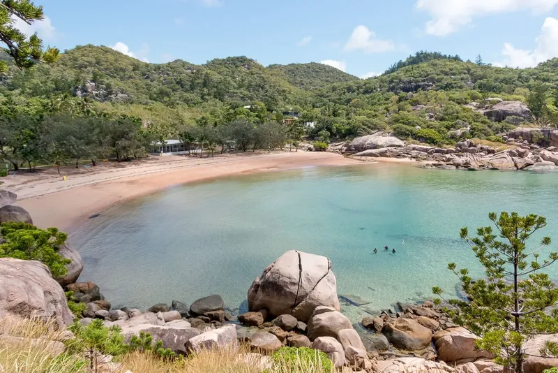 Plage de sable rose avec quelques personnes dans l'eau turquoise