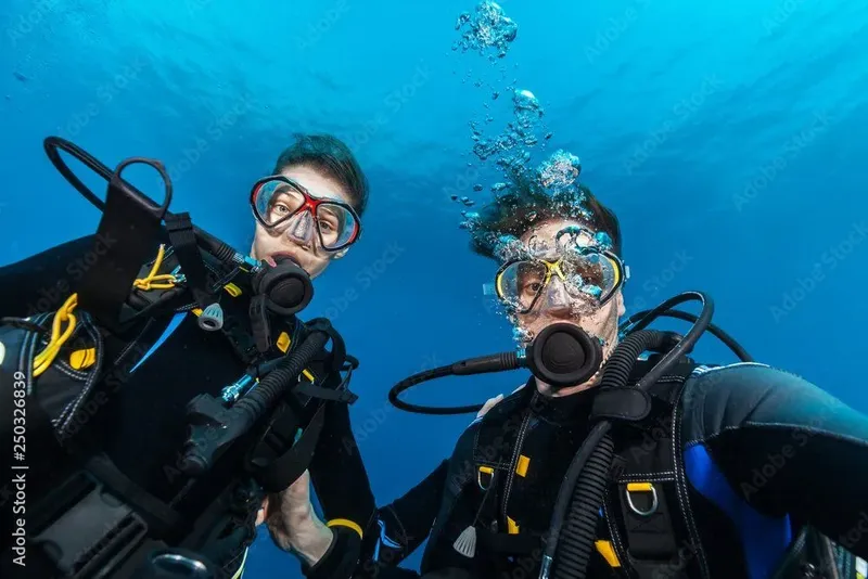 Deux plongeurs souriants avec leur équipement complet sous l'eau
