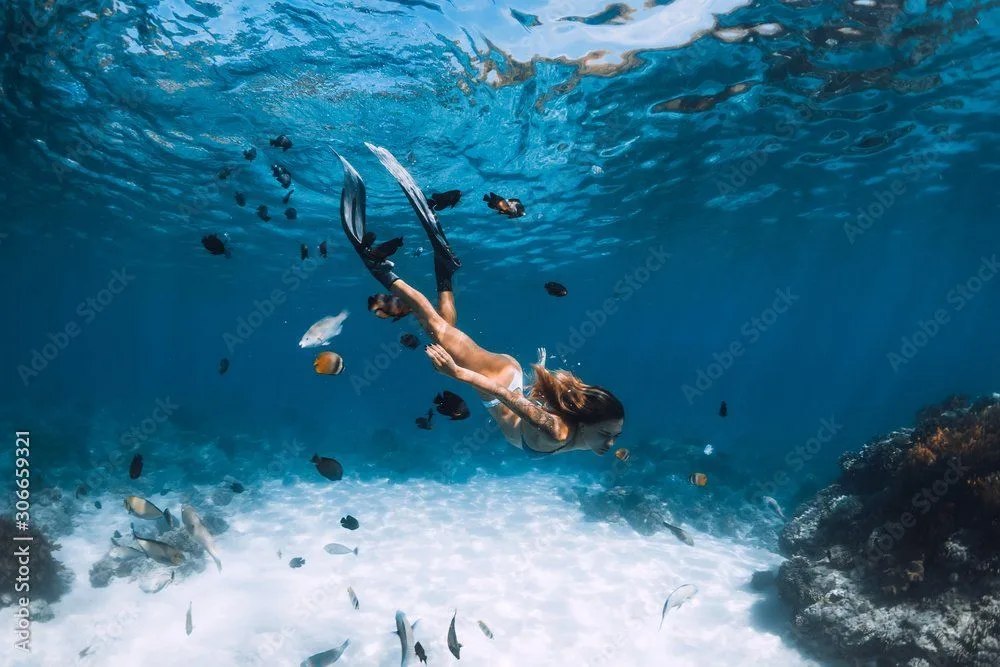 Femme nageant en apnée dans une eau turquoise claire et ensoleillée