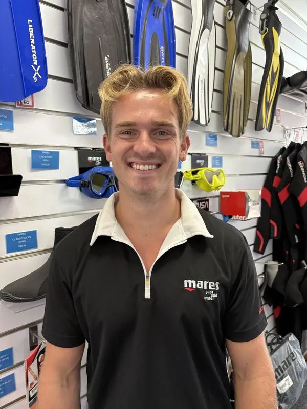 Un homme souriant dans un magasin de plongée entouré de matériel