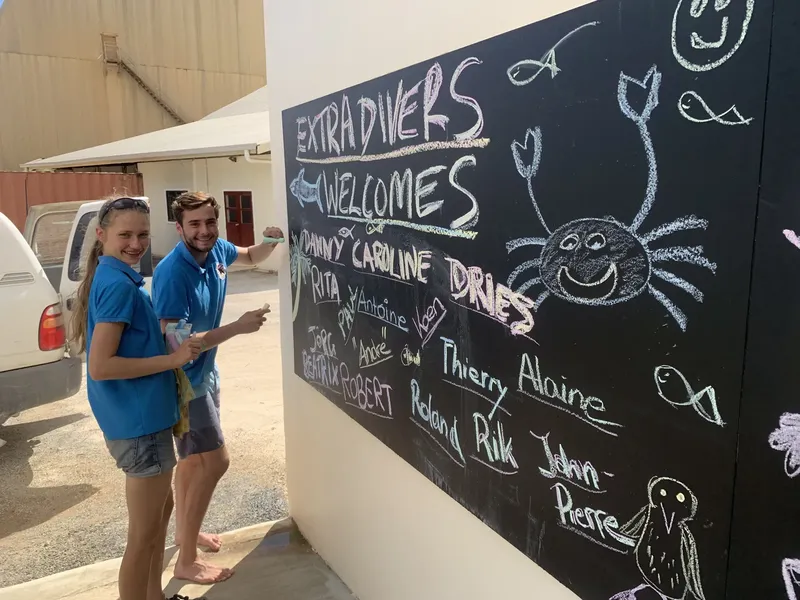 Deux personnes souriantes devant un tableau noir avec des noms