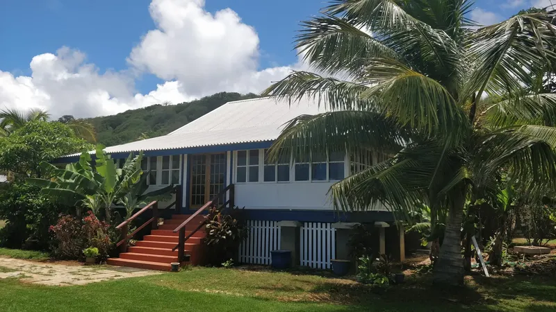 Bâtiment blanc et bleu avec escalier rouge, végétation tropicale, ciel nuageux