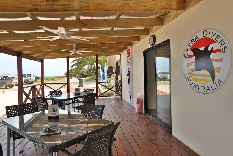 Terrasse ombragée avec tables, chaises et logo de centre de plongée