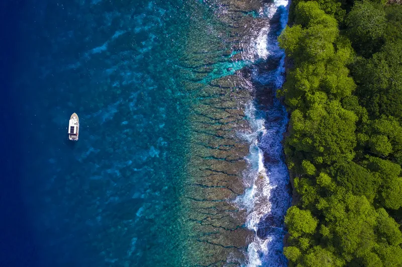 Vue aérienne d'un bateau au large d'une côte rocheuse et verdoyante