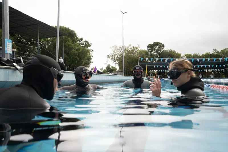 Quatre personnes en combinaison de plongée discutent dans une piscine