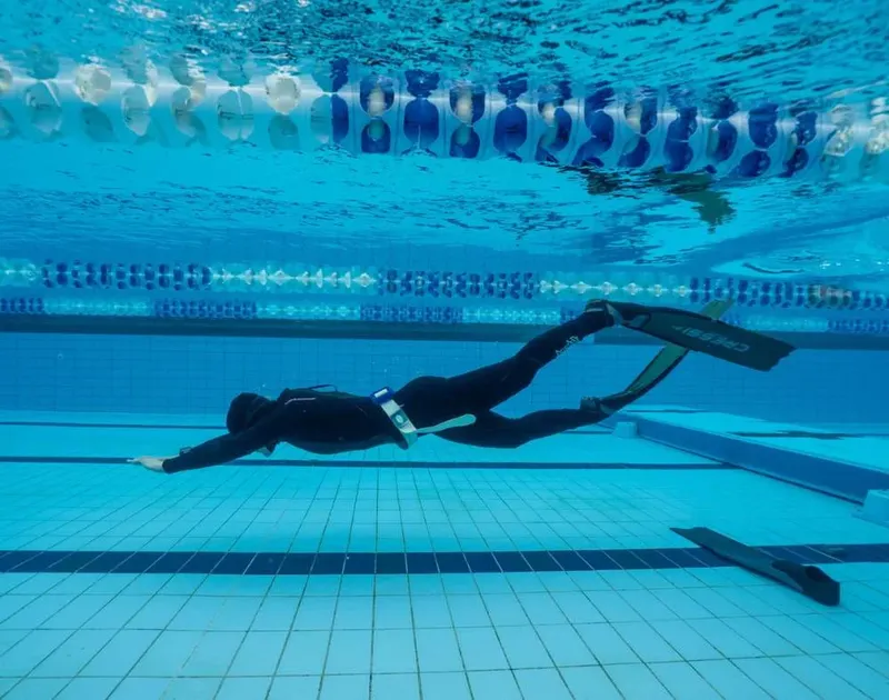Apnée en piscine : nageur en combinaison noire, palmes orange