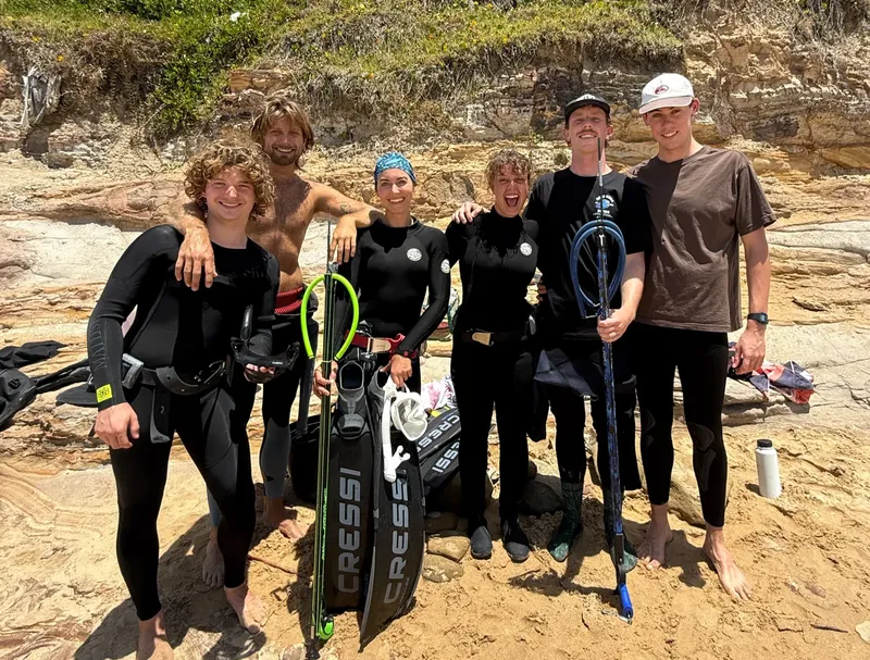 Groupe de personnes souriantes en combinaison de plongée sur une plage