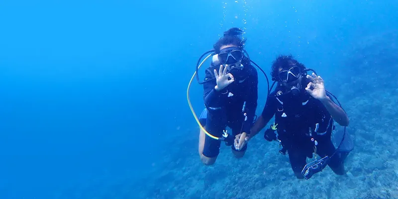 Deux plongeurs souriants font des signes de la main sous l'eau
