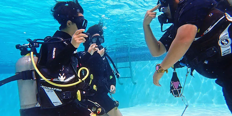 Trois plongeurs en formation communiquent sous l'eau dans une piscine
