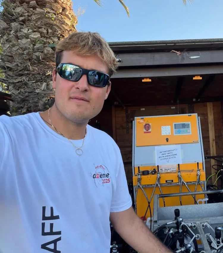 Un homme souriant porte des lunettes de soleil et un t-shirt blanc