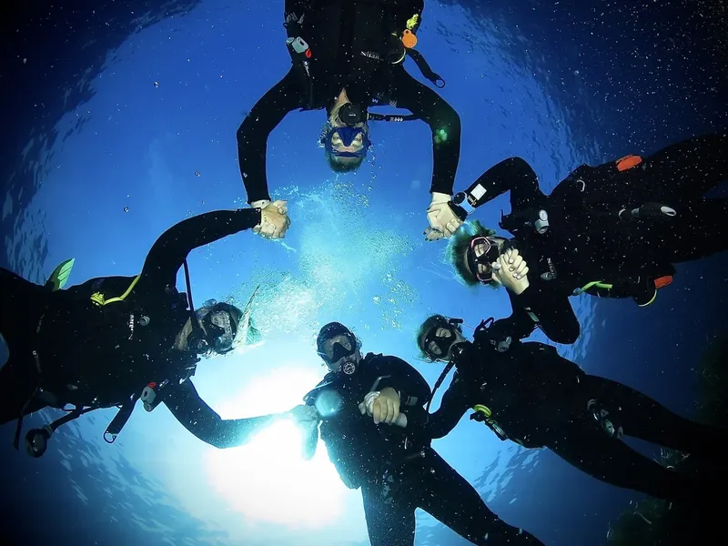 Groupe de plongeurs souriants formant un cercle sous la surface de l'eau