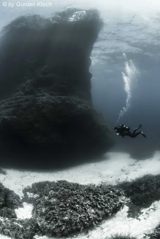 Plongeur explorant une formation rocheuse sous-marine, lumière diffuse et sable