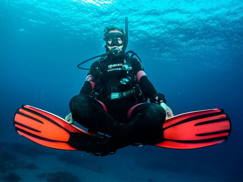 Plongeuse en combinaison noire et orange, flottant dans l'eau bleue