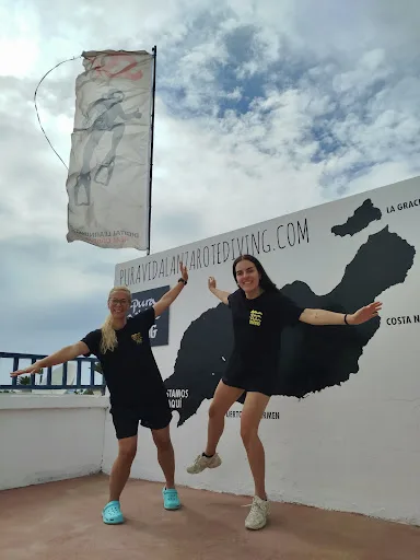 Deux femmes souriantes posent devant un mur avec une carte et un drapeau