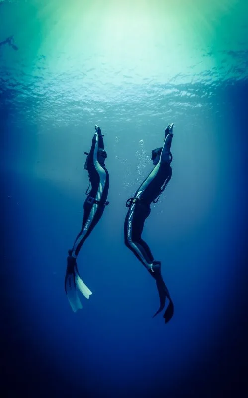 Deux plongeurs en apnée évoluent dans une eau bleue et lumineuse