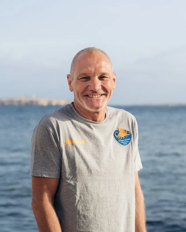 Homme souriant, portrait en extérieur, mer en arrière-plan, t-shirt bleu