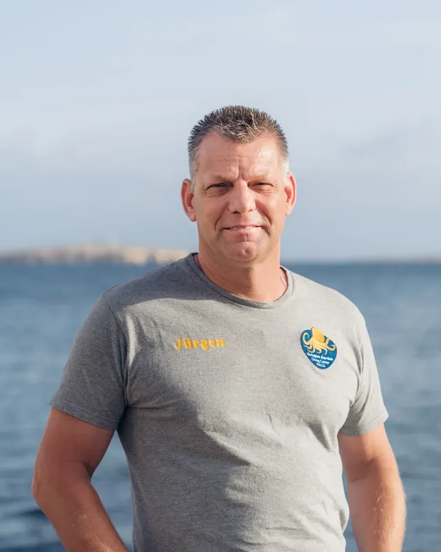 Homme souriant regardant la caméra, portant un polo gris et bleu