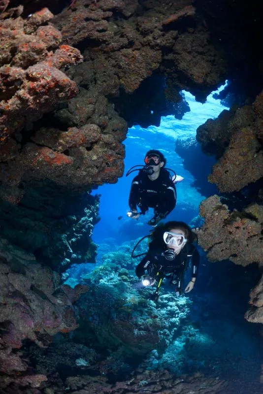 Deux plongeurs explorent une grotte sous-marine avec une lumière bleutée