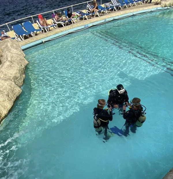Trois plongeurs en formation dans une piscine, instructeur expliquant