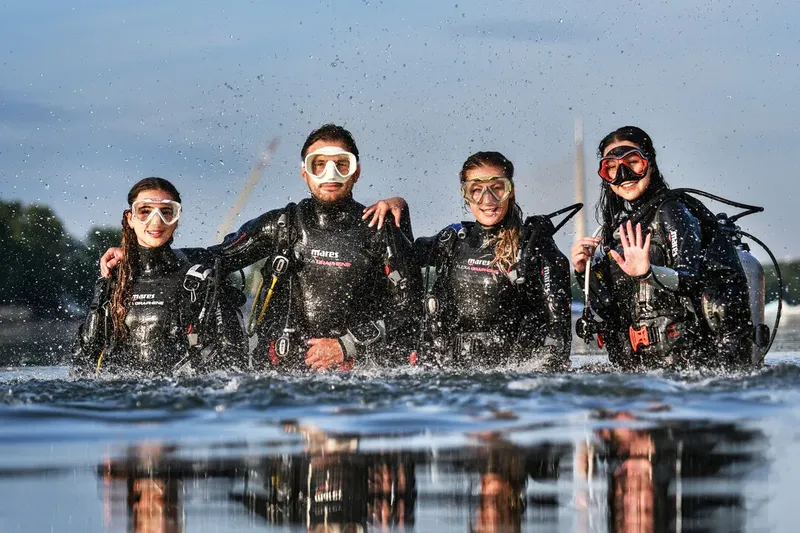Quatre plongeurs souriants en combinaison sortent de l'eau ensemble
