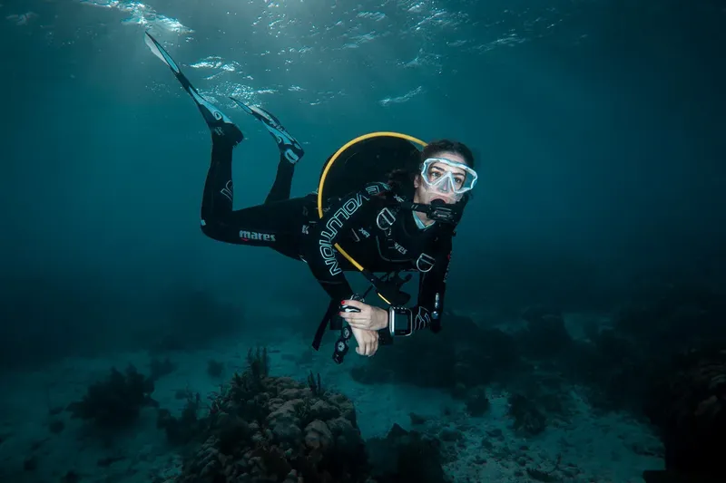 Plongeuse en combinaison noire nageant dans une eau bleue claire