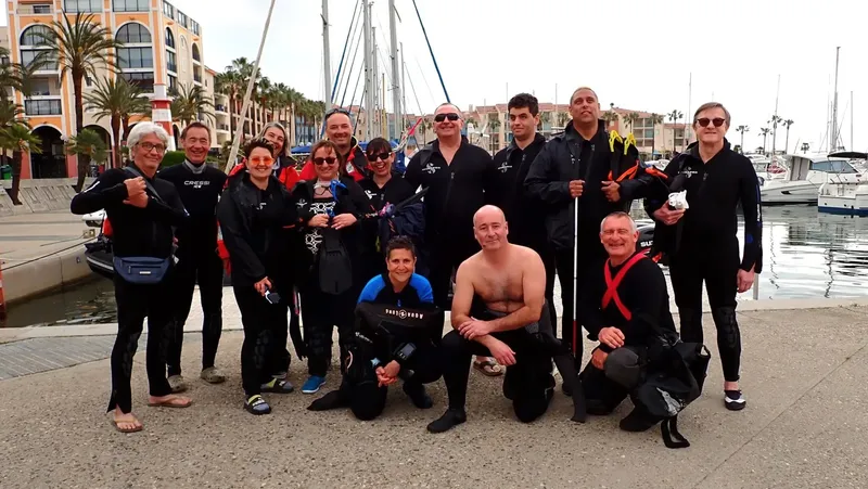Groupe de plongeurs souriants posant sur un quai ensoleillé près des bateaux