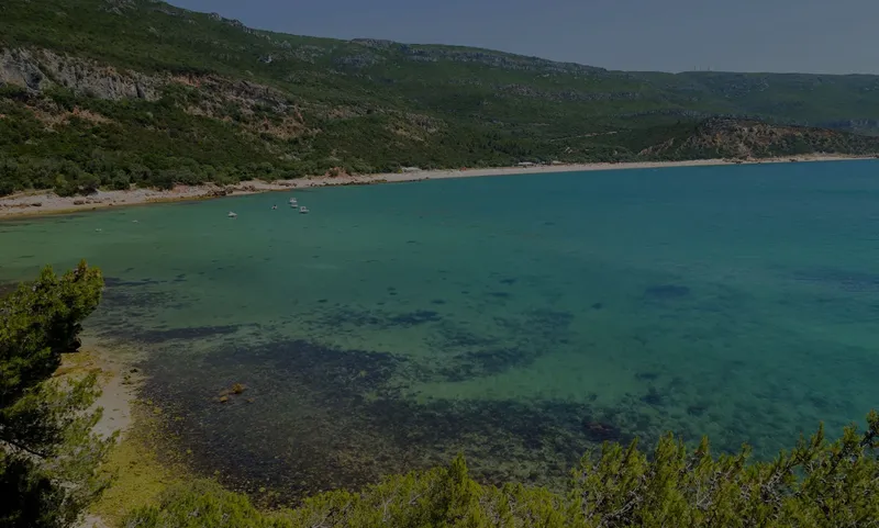 Cote rocheuse surplombant une crique turquoise avec quelques bateaux amarrés