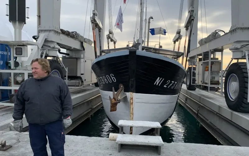 Homme debout devant un bateau à quai, hiver, ciel gris