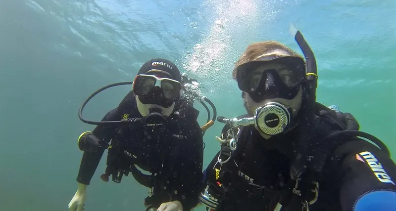 Deux plongeurs souriants avec leur équipement complet sous l'eau