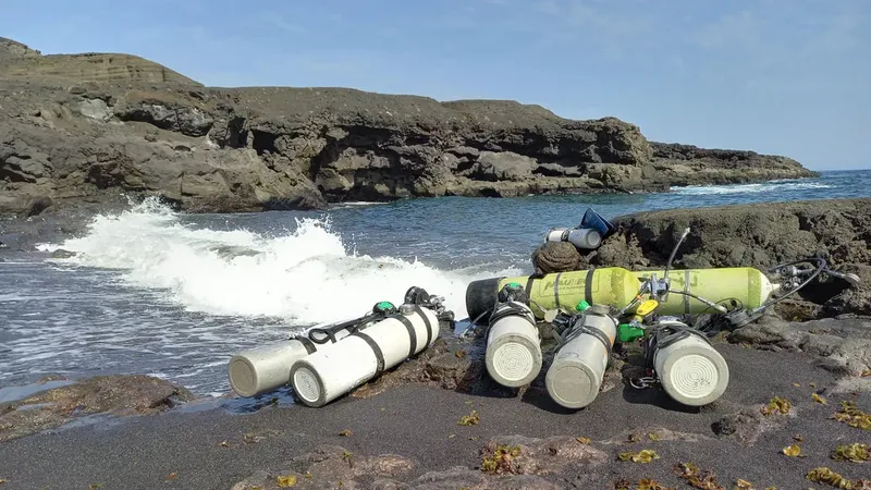Bouteilles de plongée sur une plage de sable noir avec vagues et rochers