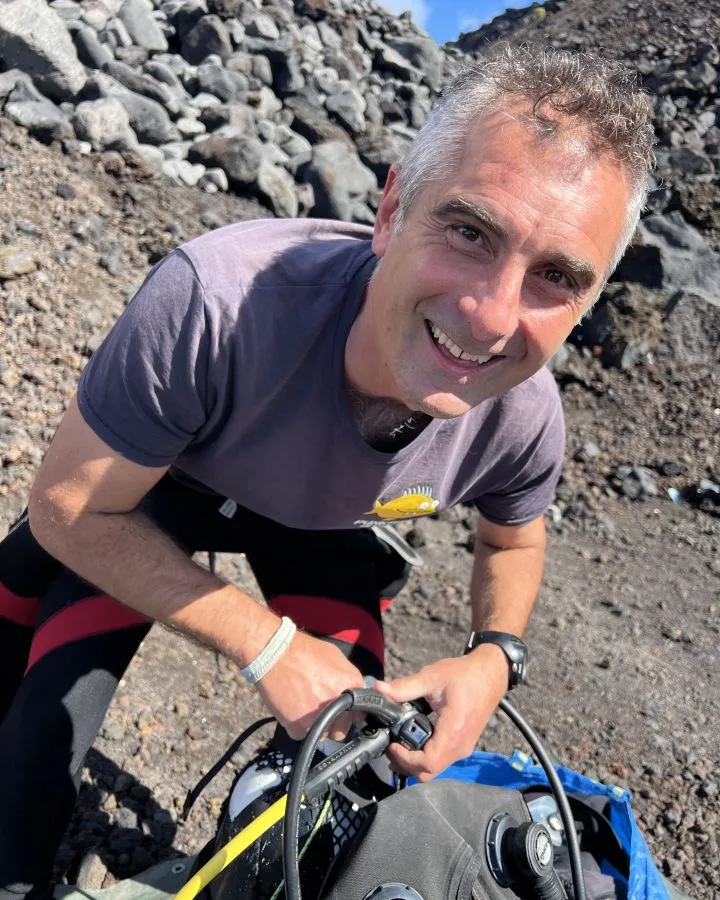 Plongeur souriant avec son équipement sur un fond rocheux