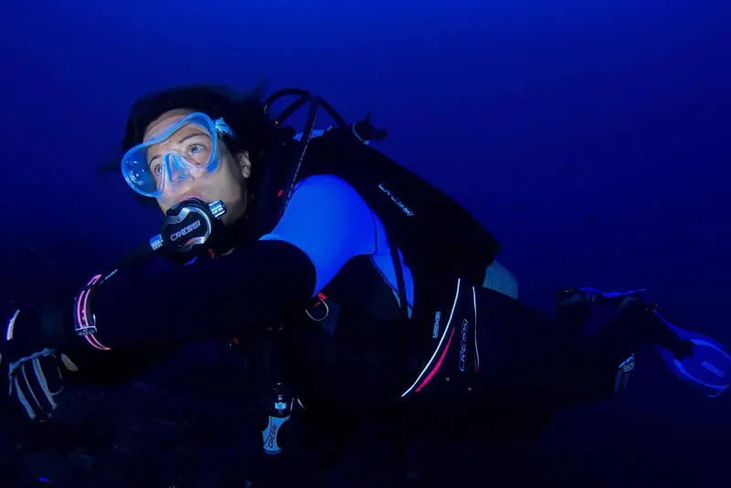 Plongeur en combinaison regarde vers la camera dans l'eau bleue