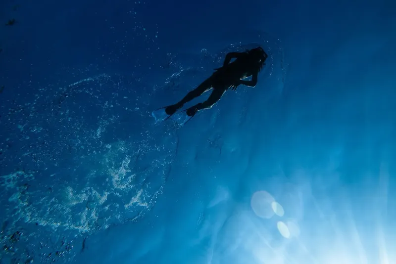 Plongeuse silhouettée nageant dans une eau bleue et lumineuse