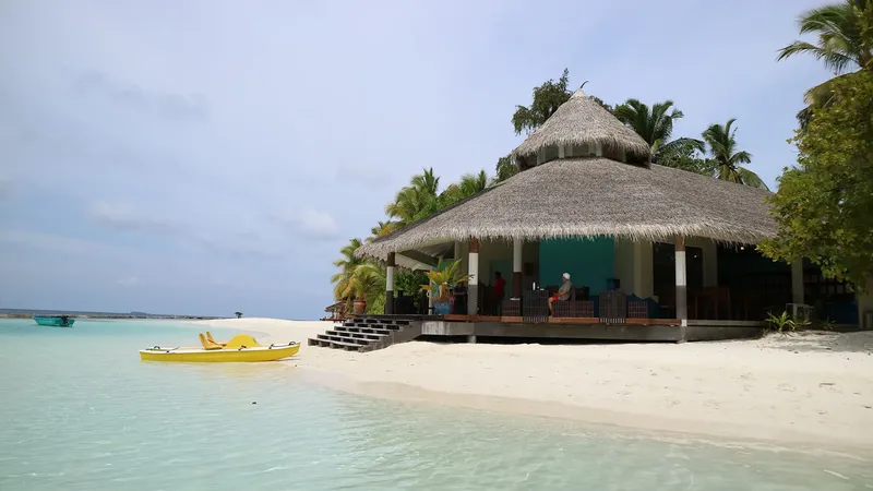 Plage de sable blanc, bâtiments avec toits de chaume, personnes assises
