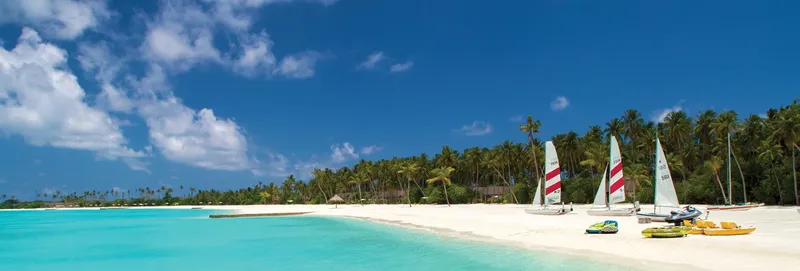 Plage de sable blanc, mer turquoise, voiliers et kayaks sous le soleil