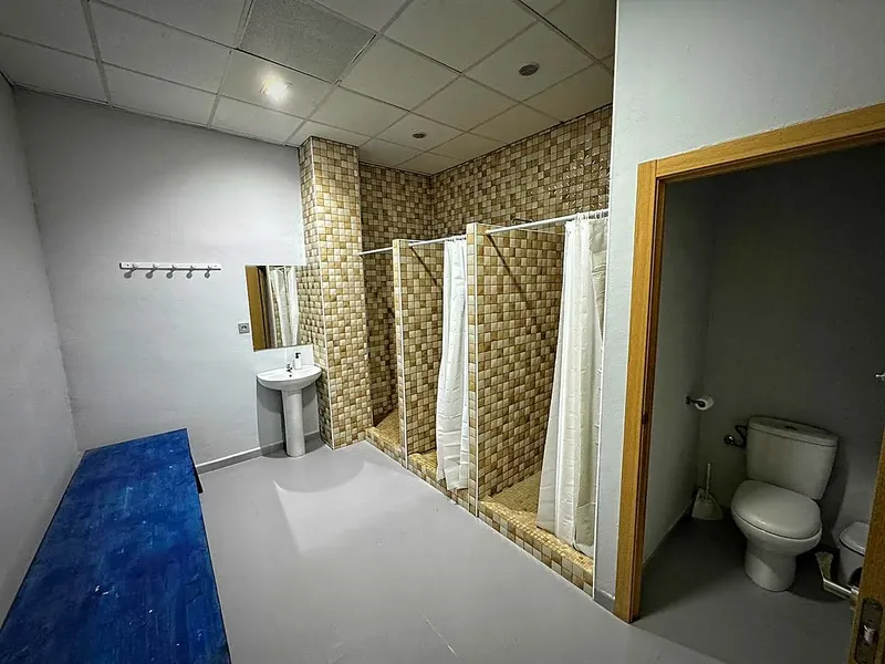 Vestiaires avec douches, lavabo et banc bleu dans une pièce claire