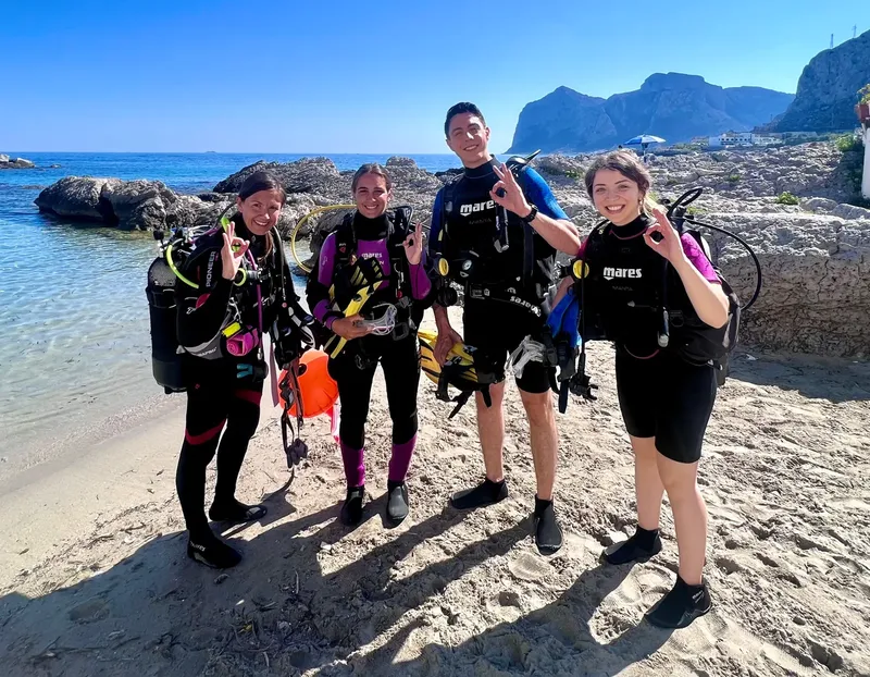 Quatre plongeurs souriants en combinaison sur une plage ensoleillée