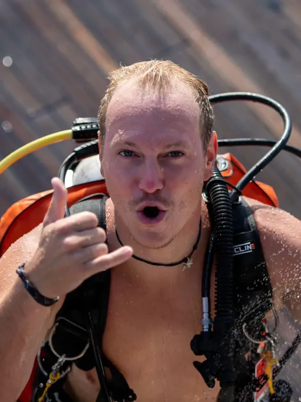 Plongeur souriant avec signe OK, équipé, sur un ponton en bois