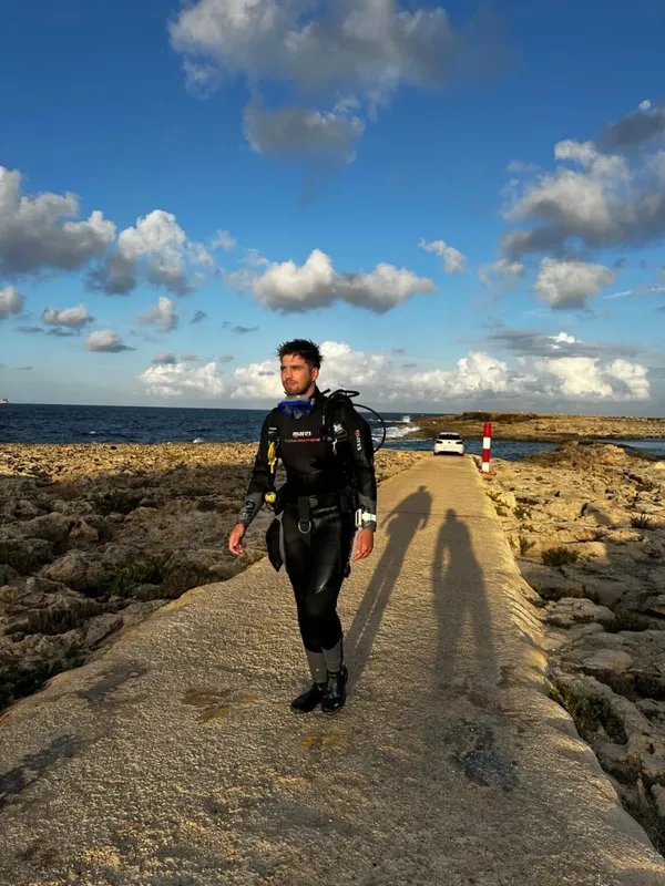 Plongeur en combinaison marchant sur un chemin rocheux près de la mer