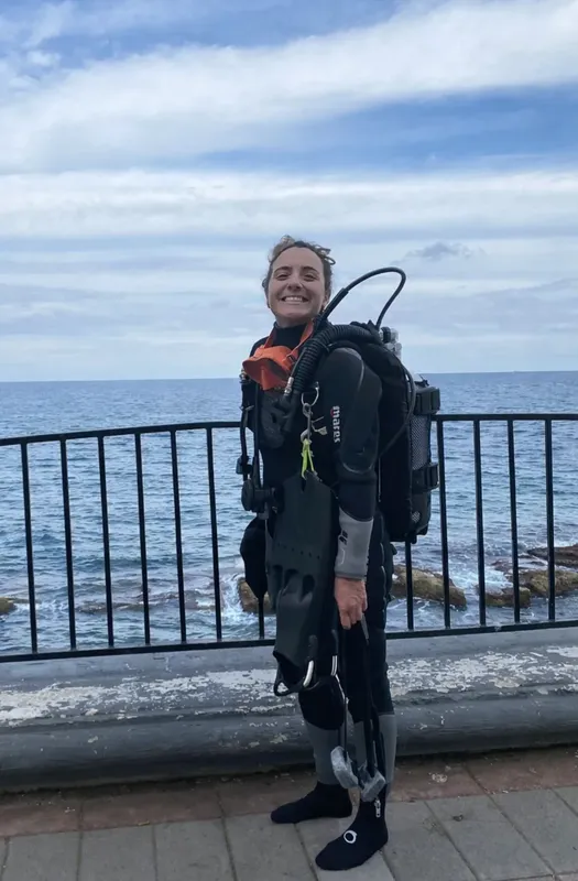 Plongeuse souriante en combinaison complète, équipée, devant la mer