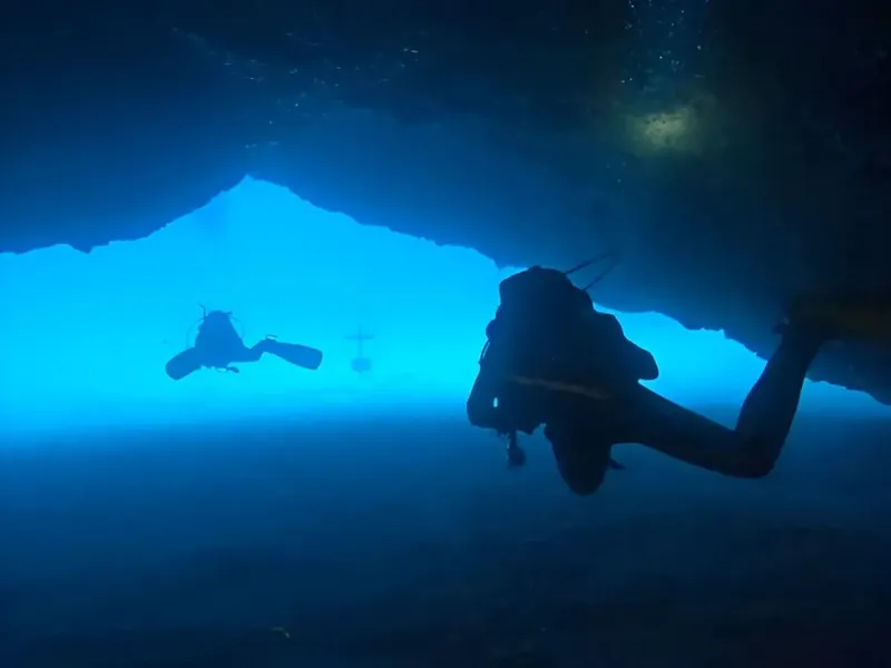 Deux plongeurs explorent une grotte sous-marine, lumière bleue ambiante